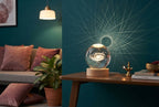 A 3D crystal lamp ball glowing on a wooden table, casting geometric light patterns in a modern living room with deep teal wal